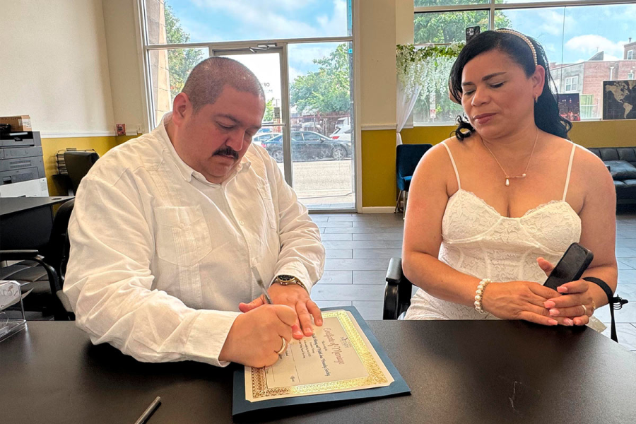 Un hombre y una mujer sentados en una mesa firmando un acta notarial de matrimonio en New Jersey